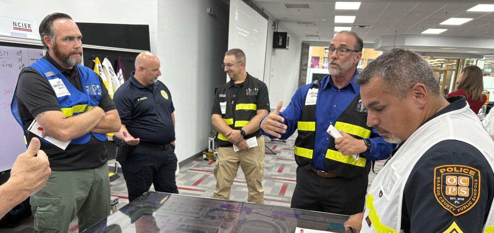 School district police, law enforcement, fire and EMS participants and an NCIER instructor around a digital map table during a SSAVEIM Train-the-Trainer delivery.