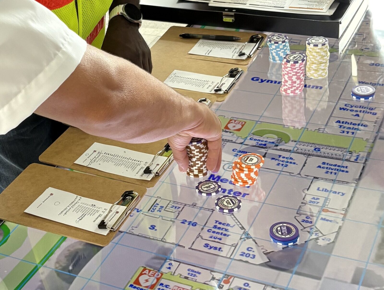 A paramedic places resource chips on a Counterstrike Terrain digital map table during a SSAVEIM scenario, with classroom rosters on clipboards alongside.